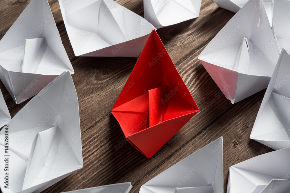 Business leadership concept with white and color paper boats on wooden table