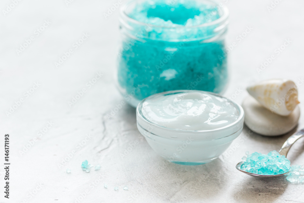 blue bath salt, body cream and shells for spa on white table background