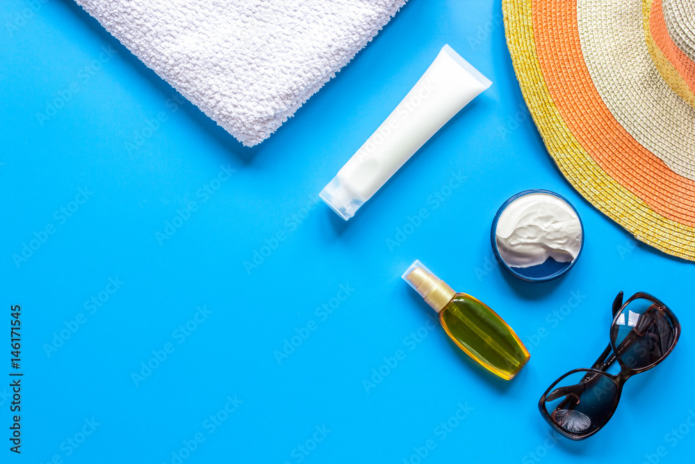 Sun protection composition with glasses and cream on blue background top view mockup