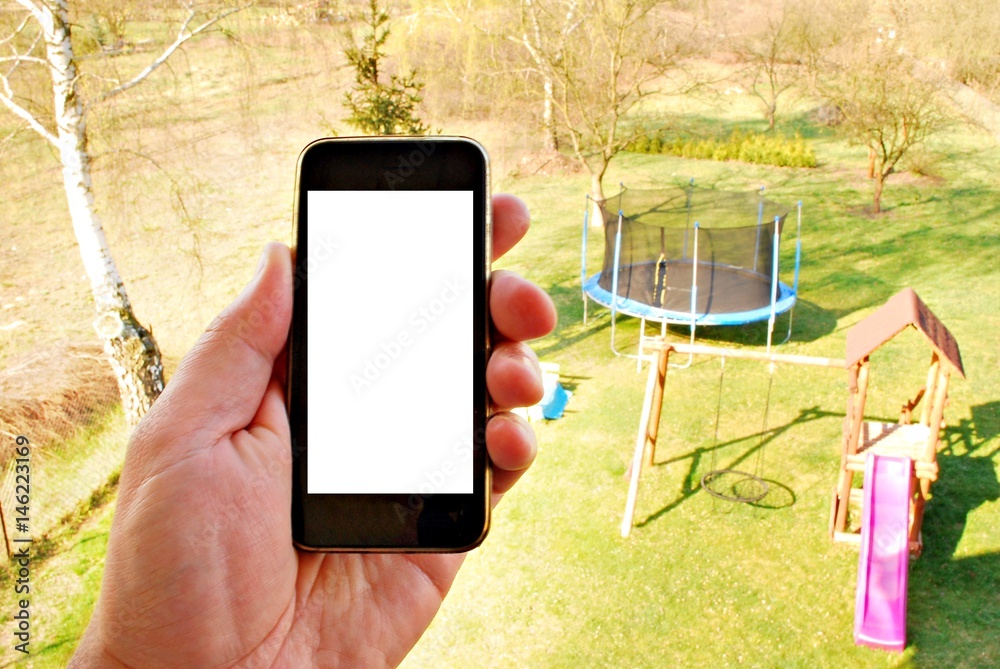 Hand holding black smartphone with blank screen against playground background