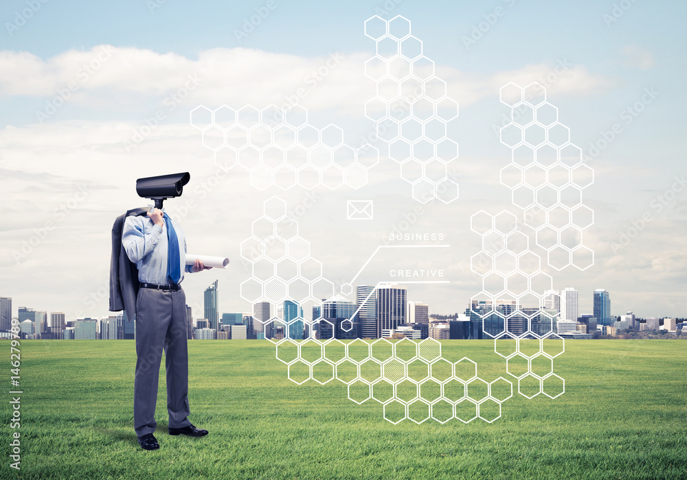 Camera headed man standing on green grass against modern citysca