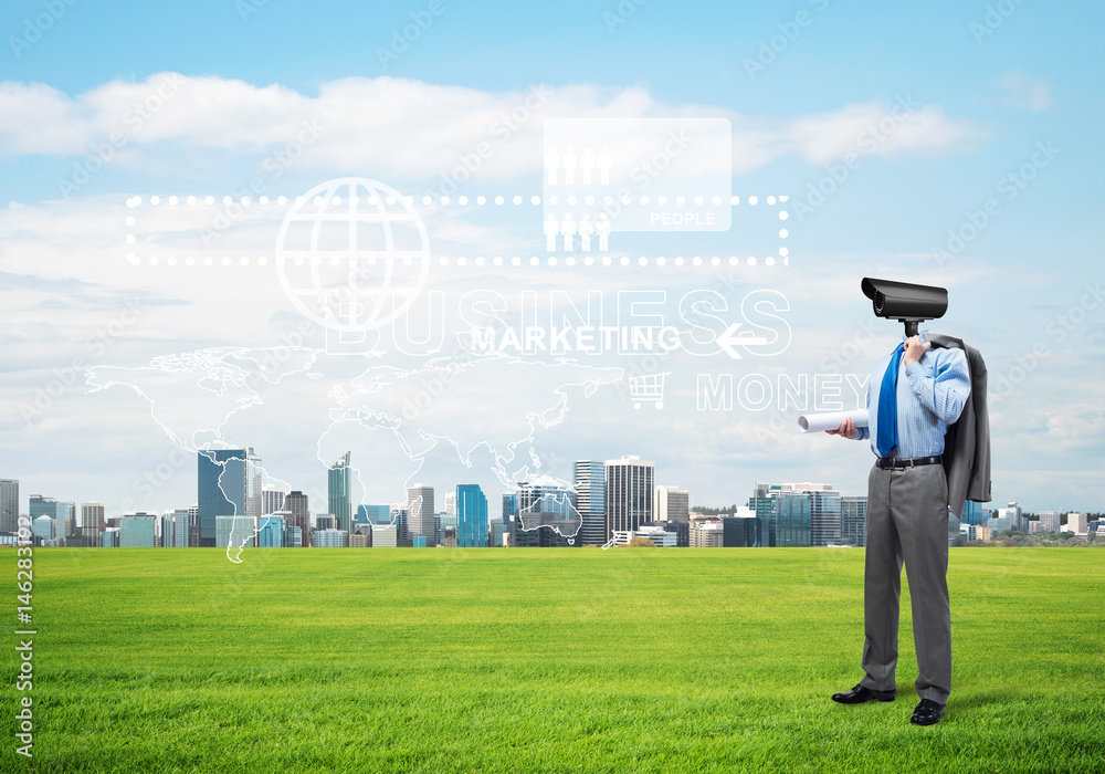 Camera headed man standing on green grass against modern cityscape