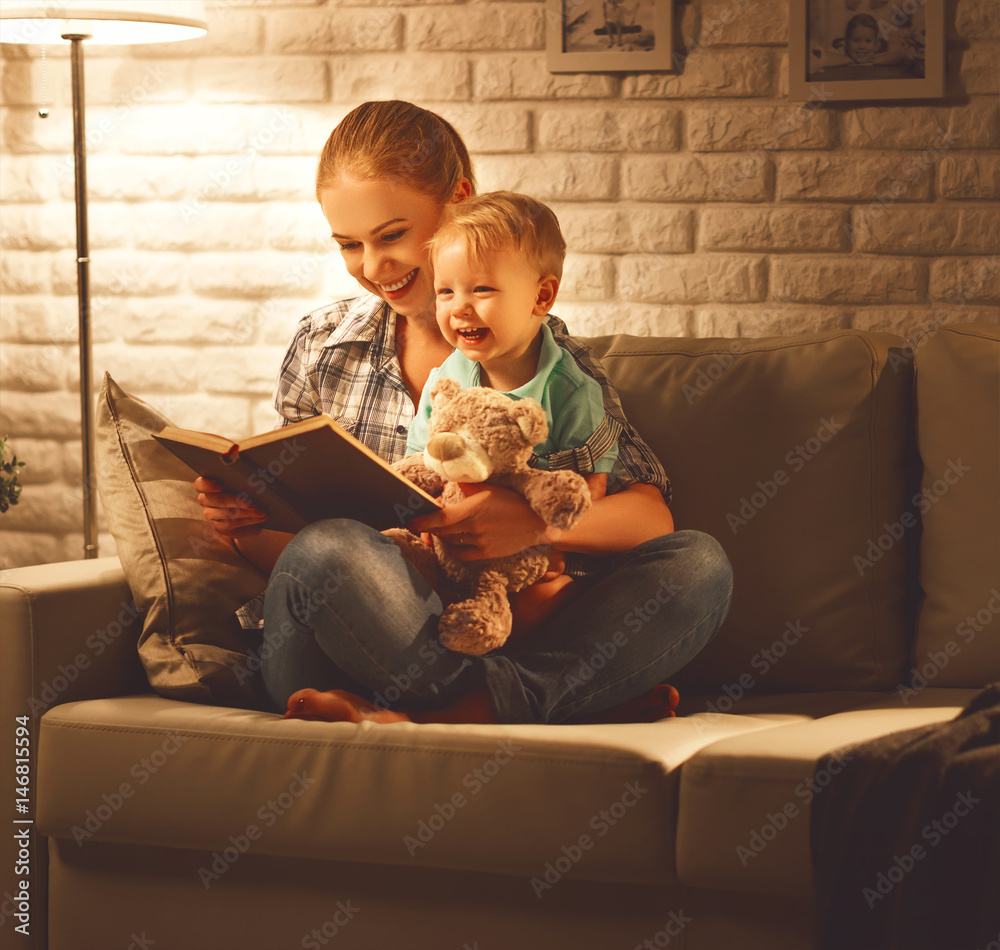 Family before going to bed mother reads to her baby son book near a lamp in the evening.