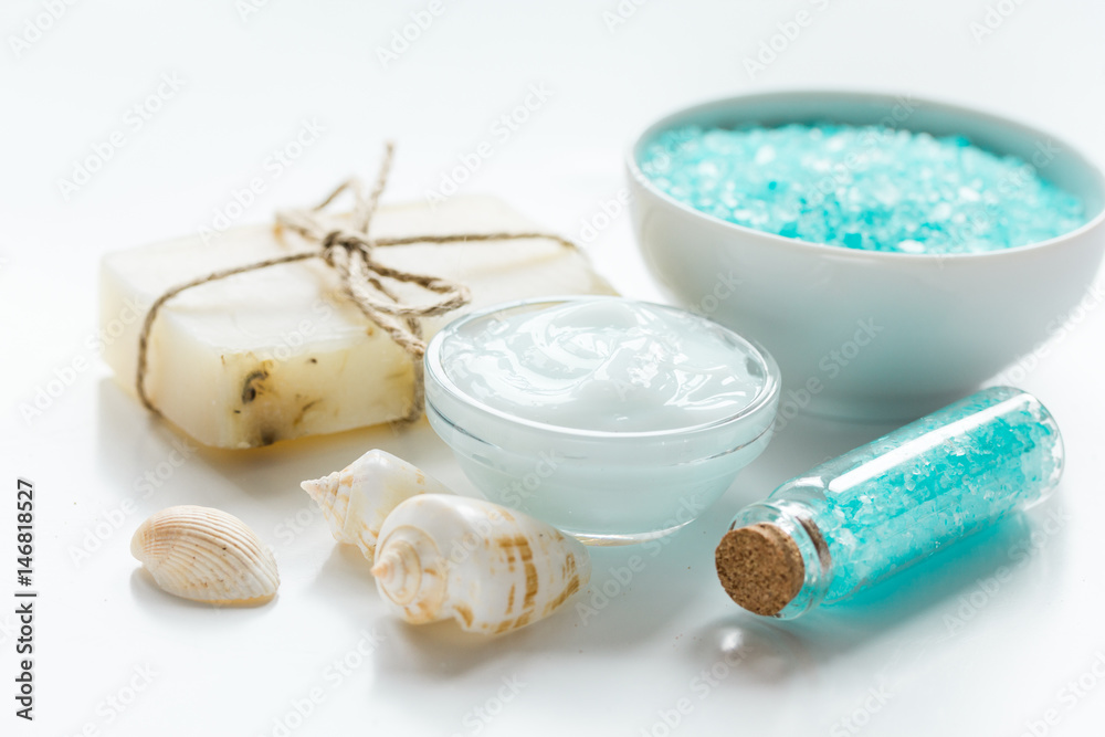 blue bath salt, body cream and shells for spa on white table background