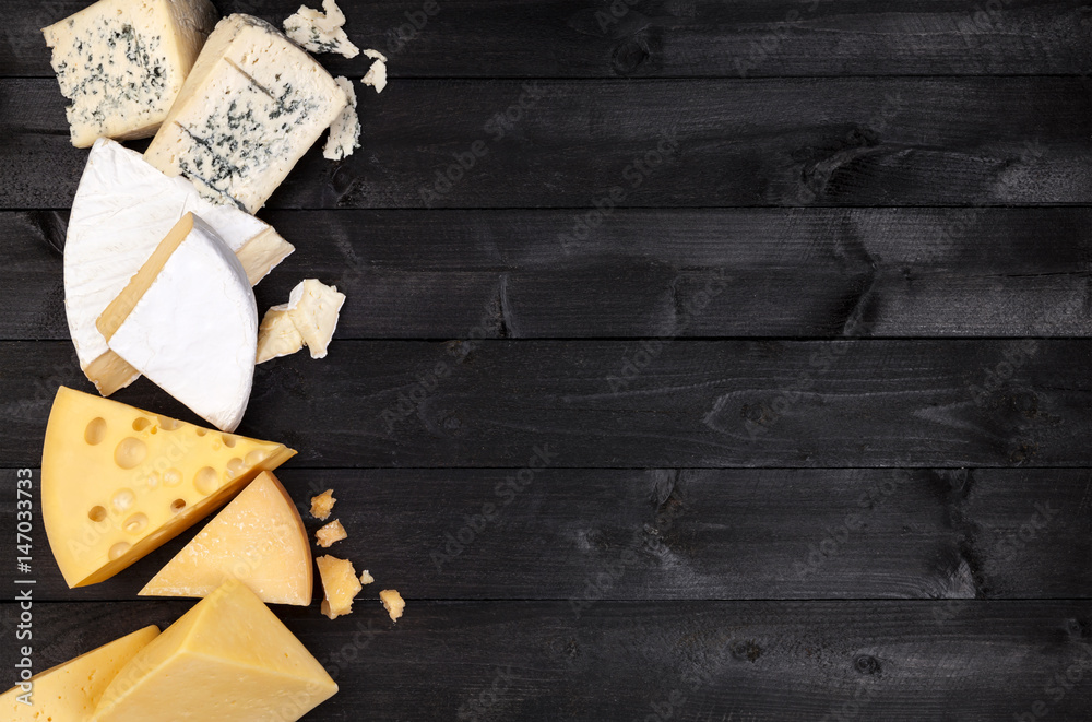 Different types of cheese on black wooden table. Top view