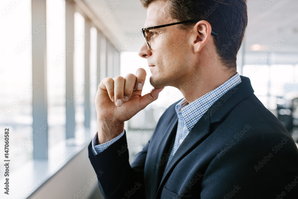 Mature businessman standing by window and thinking