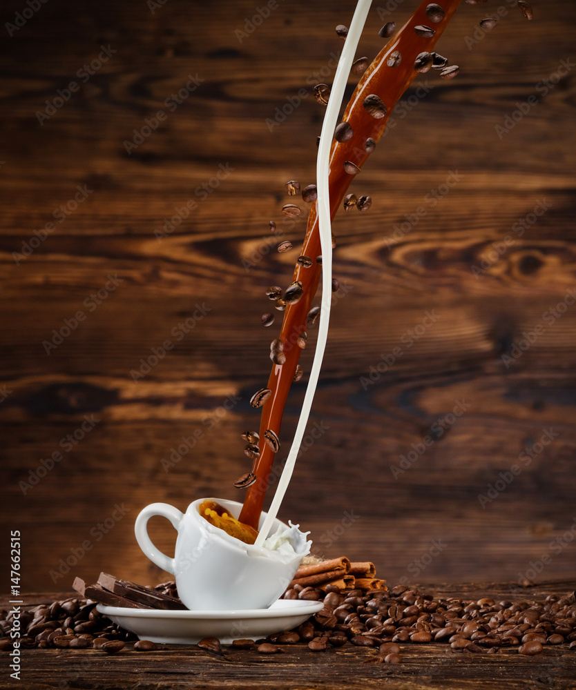 Splashing liquid of coffee and milk into white cup on wooden table