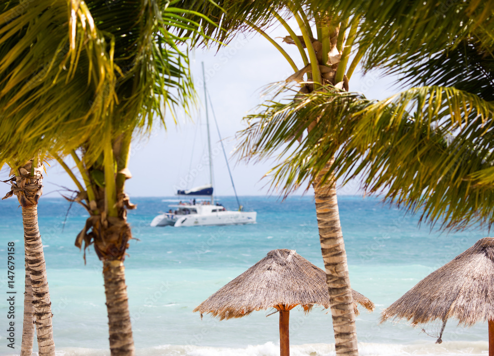 Vacation concept image. Palm trees and umbrella on the beach. Luxury yacht in the background out of 