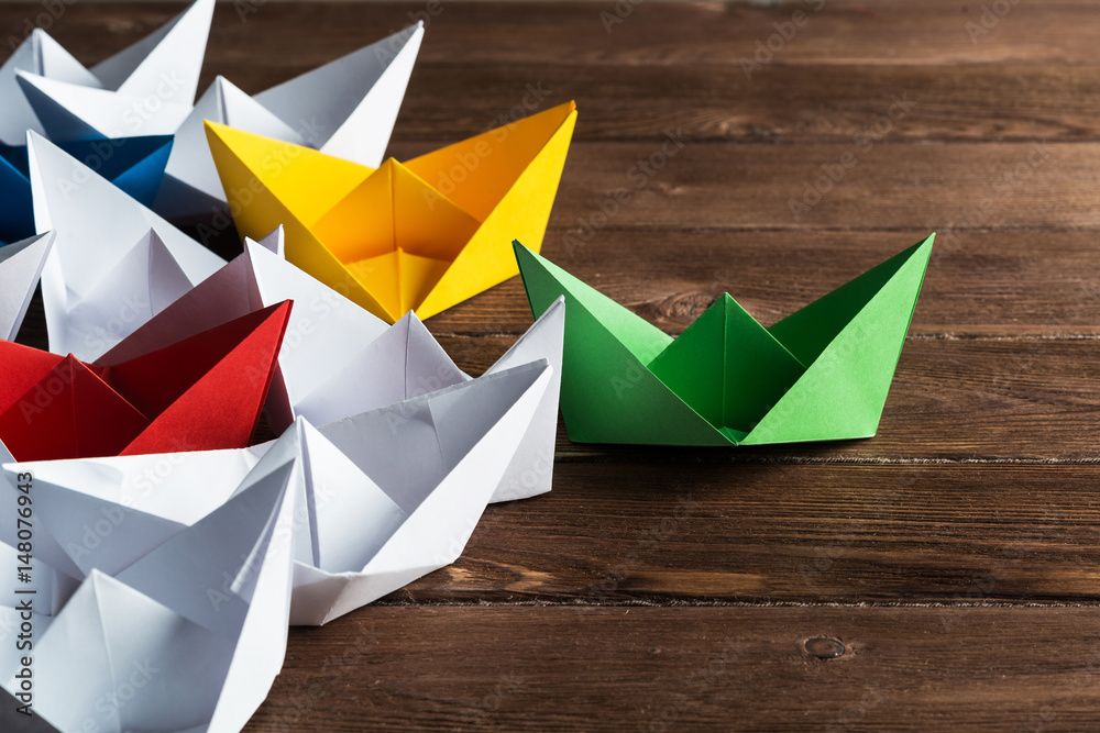 Business leadership concept with white and color paper boats on wooden table