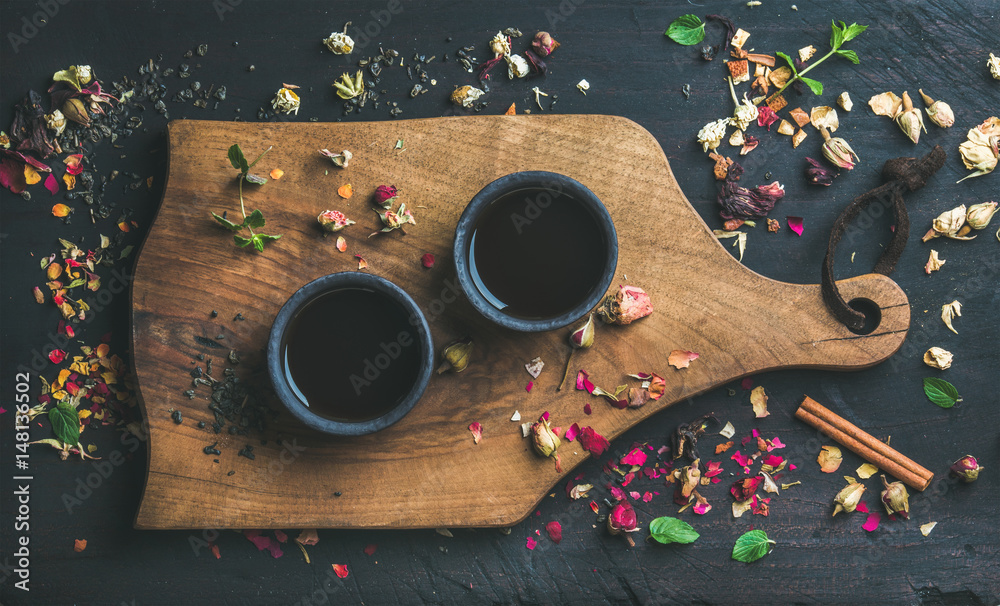 Chinese black tea in black stoneware cups on serving wooden board over black wooden background with 