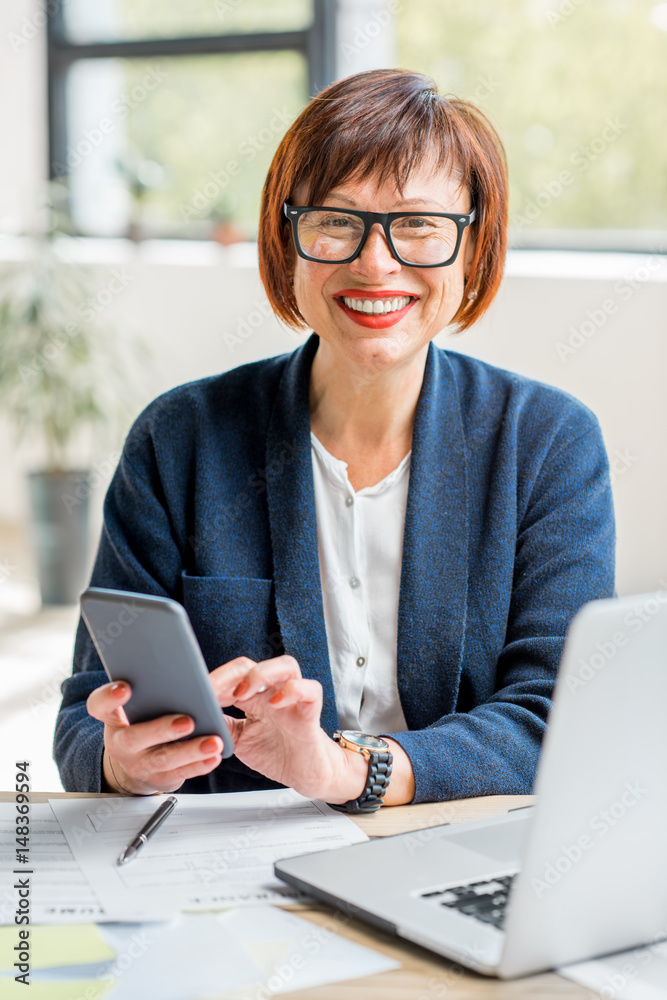 Senior businesswoman working with documents and smartphone at the bright modern office interior