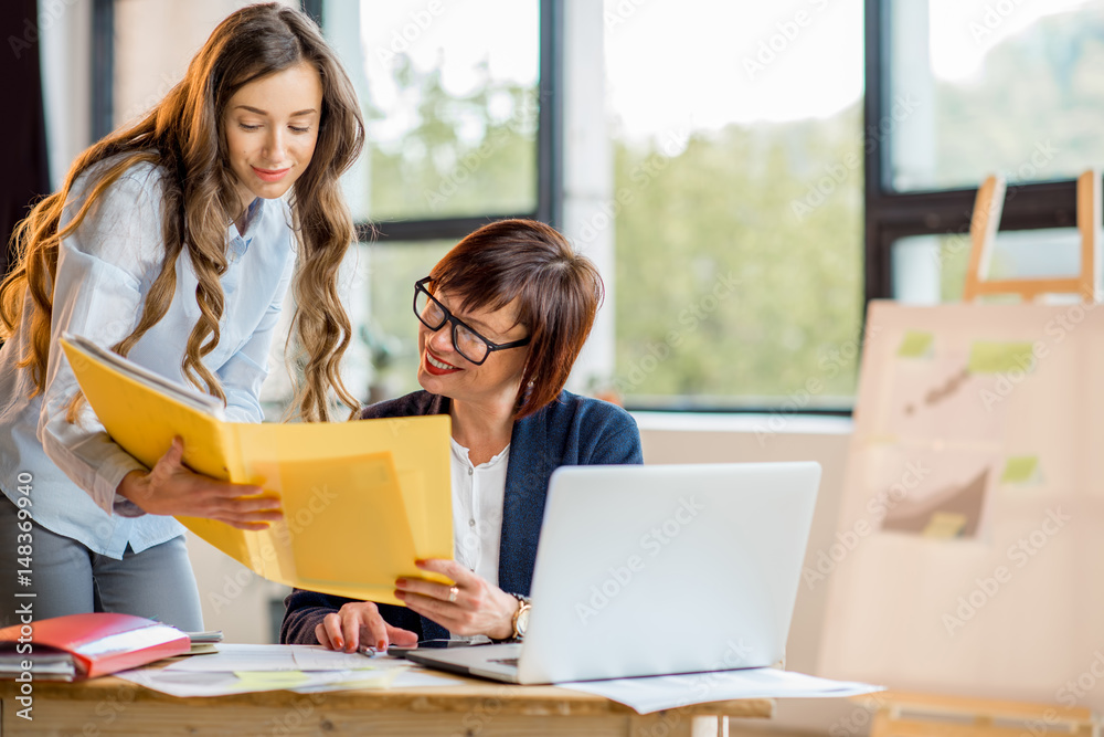 Young and older businesswomen working together on documents at the modern office interior