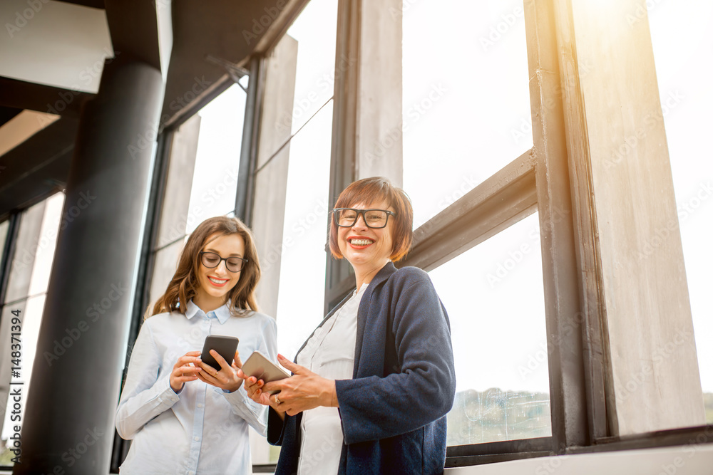 Young and older businesswomen standing near the window at the office