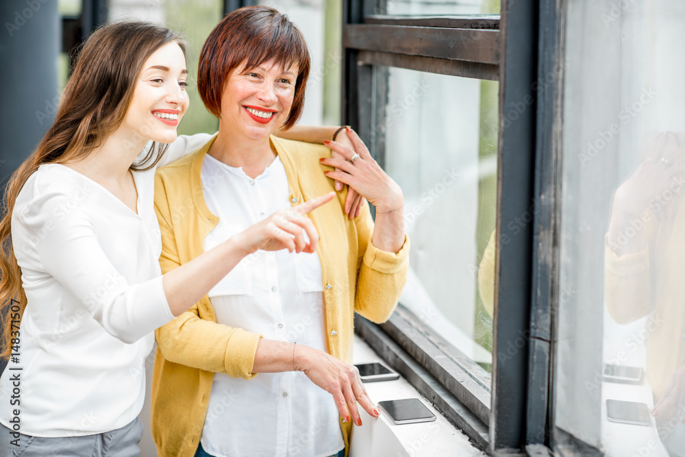 Portrait of a smiling mother and daughter standing together indoors near the window