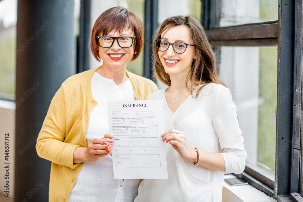 Portrait of an older happy woman with daughter holding insurance document indoors near the window