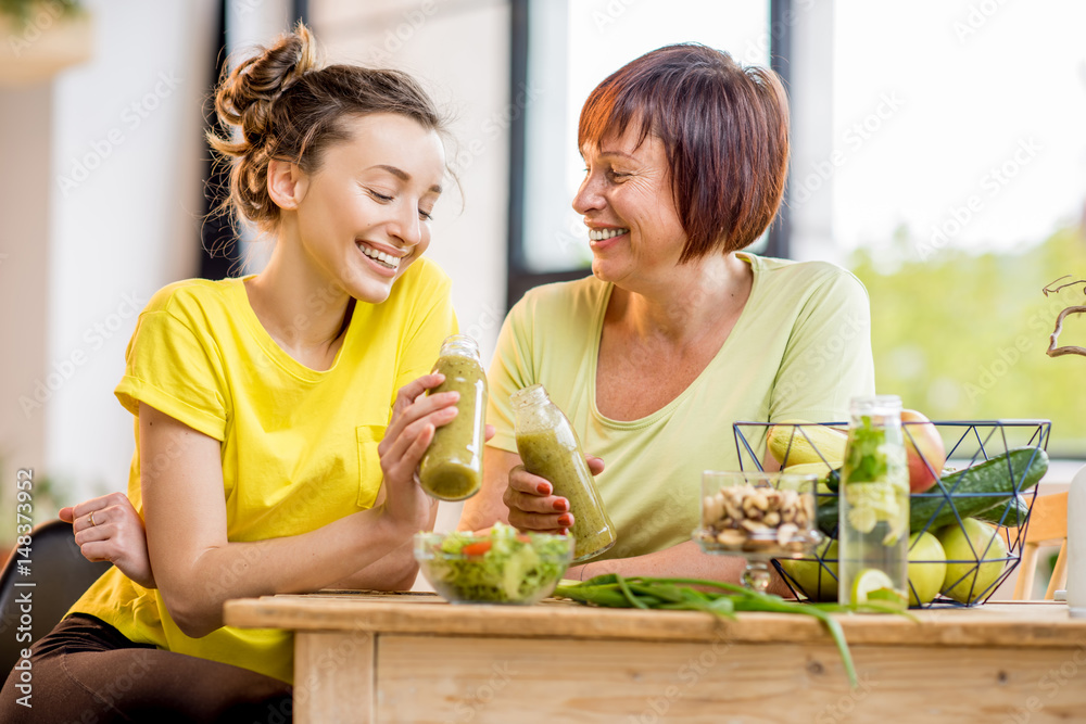 Young and older women sitting with healthy food and fresh drinks after the sports training indoors o