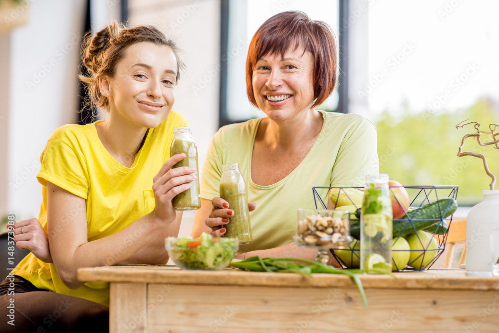 Young and older women sitting with healthy food and fresh drinks after the sports training indoors o