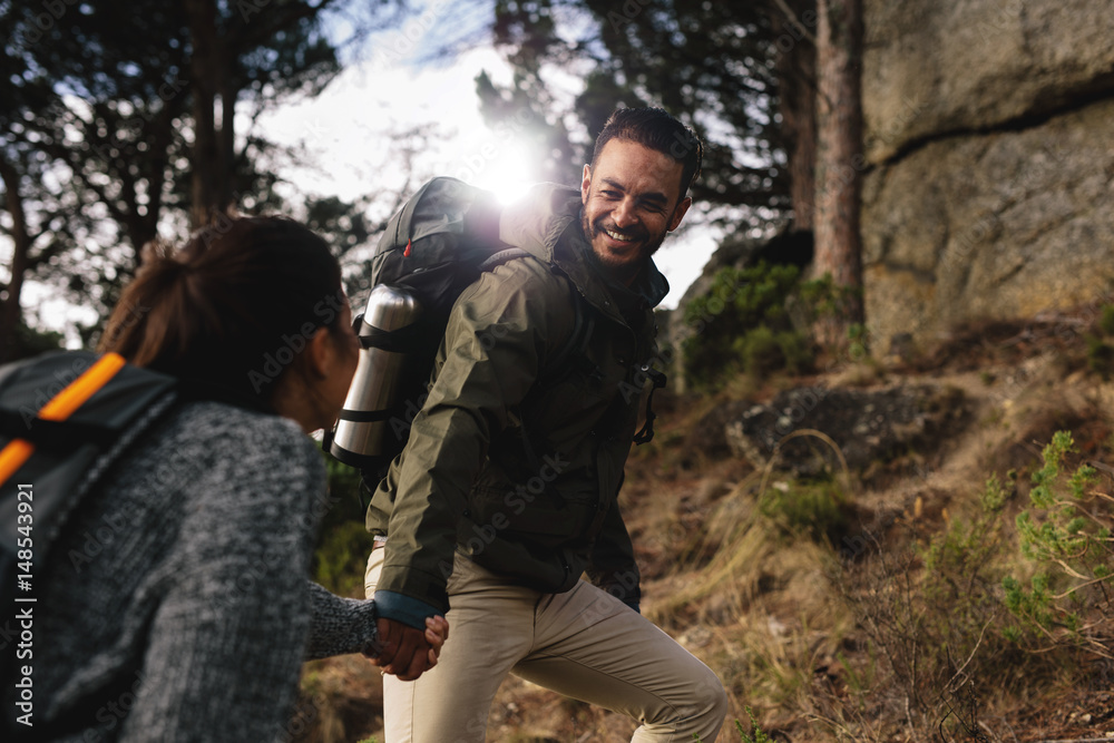 Hiker helping his girlfriend uphill on country path.