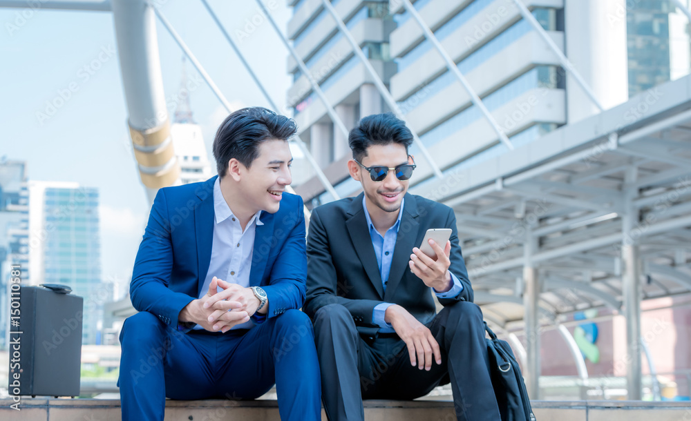 Smiling young businessman use smartphone enjoying a positive conversation talking with a mature busi