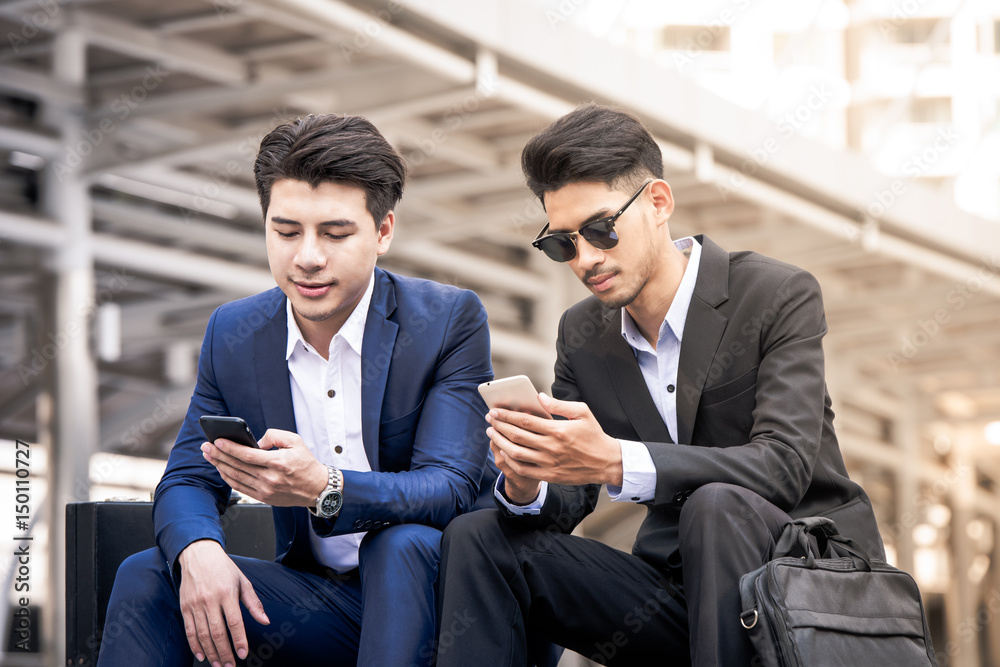 Smiling young businessman use smartphone enjoying a positive conversation talking with a mature busi