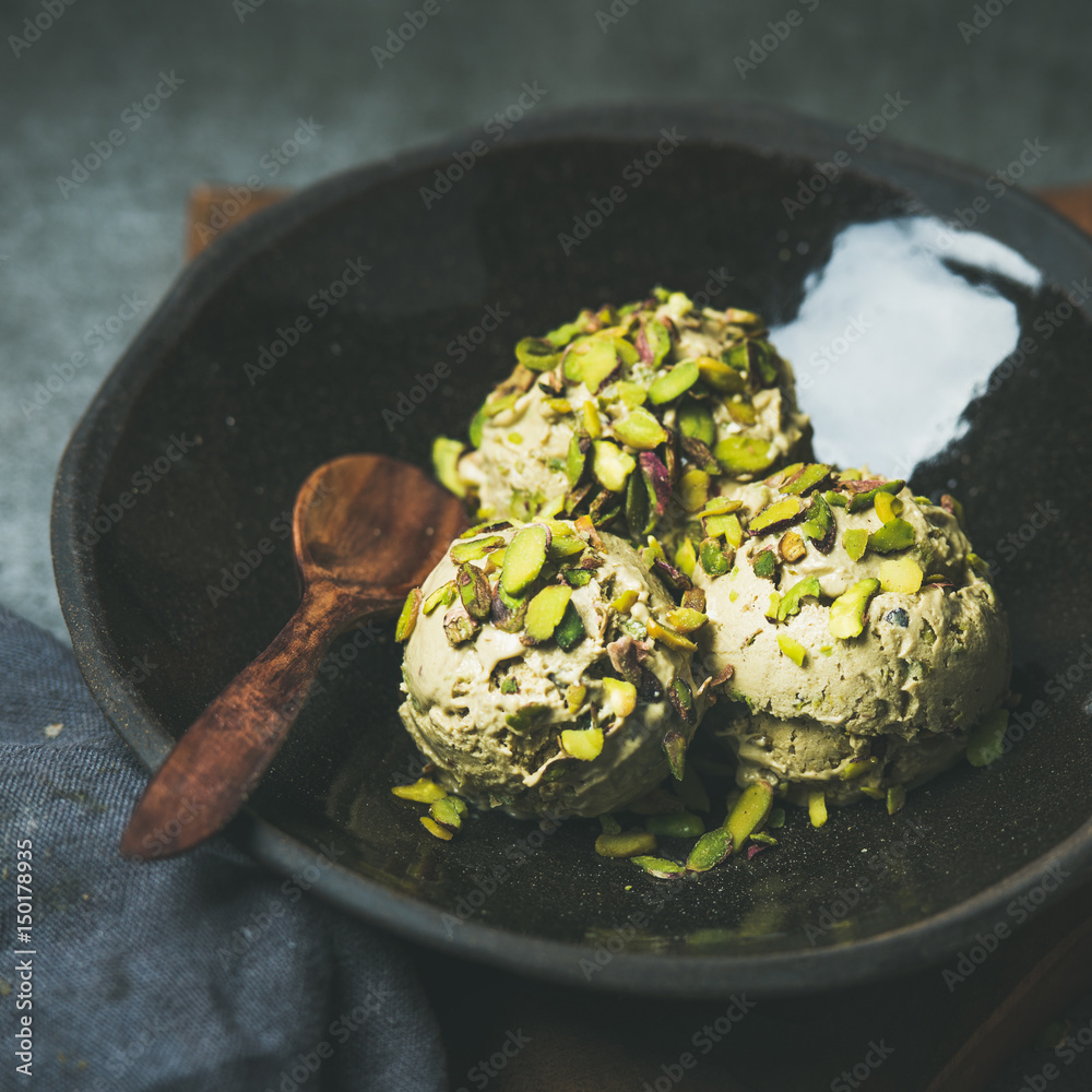 Homemade pistachio ice cream scoops with crashed pistachio nuts in dark plate over wooden board, sel