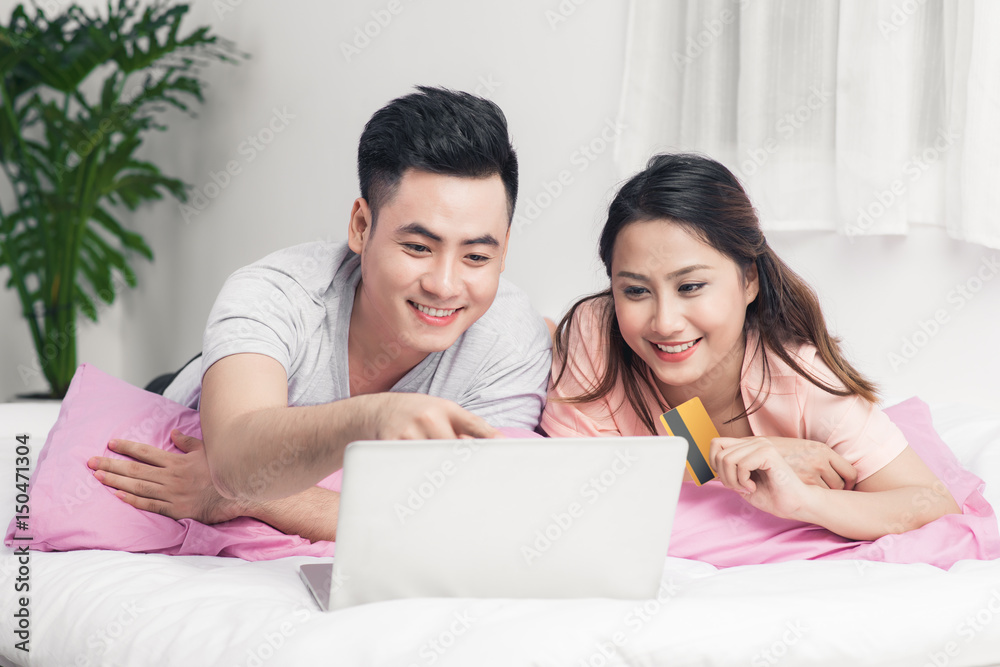 Young asian couple surfing on internet and shopping with laptop on bed.