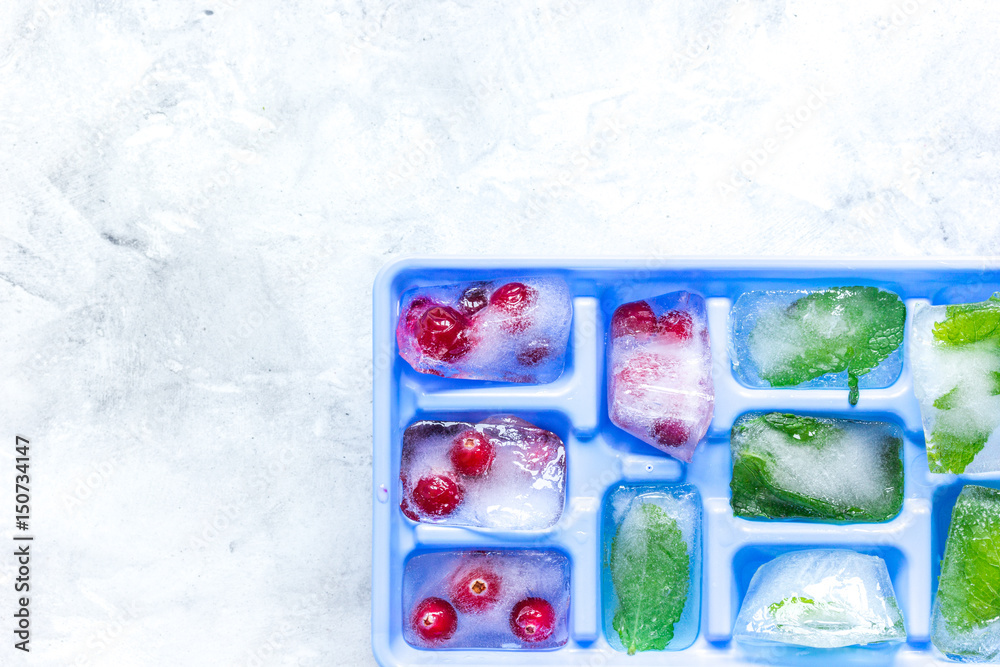 frozen red berries in ice cubes in tray on stone background space for text top view