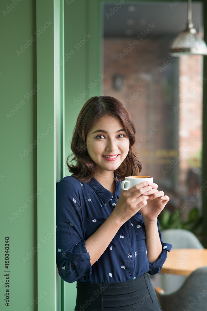 快乐的年轻商业女性的画像，手里拿着马克杯，早上在餐馆喝咖啡