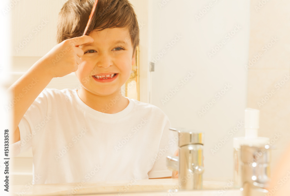 Happy kid boy combing his hair in the morning