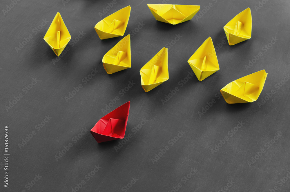 Leadership concept red leader paper boat standing out from the crowd of yellow boats