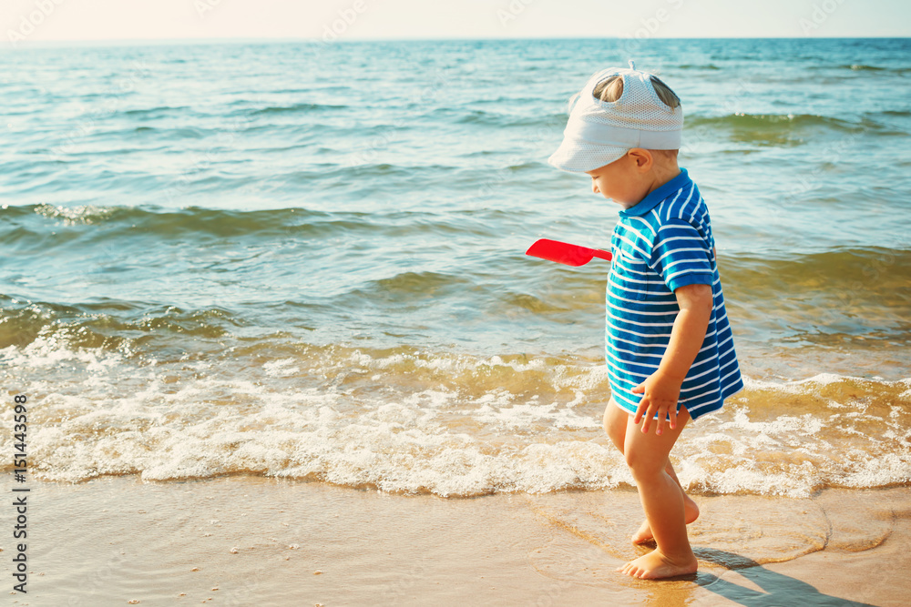 little boy walking at the beach in summer hat