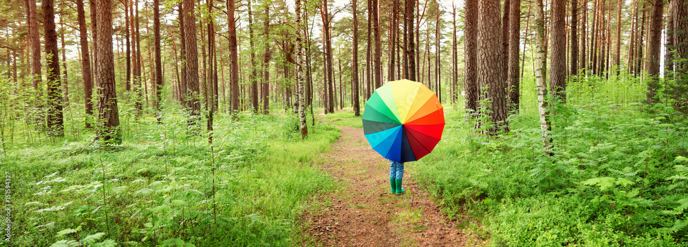 Childg in the park with colourful umbrella. Boy in rainy weather in the forest