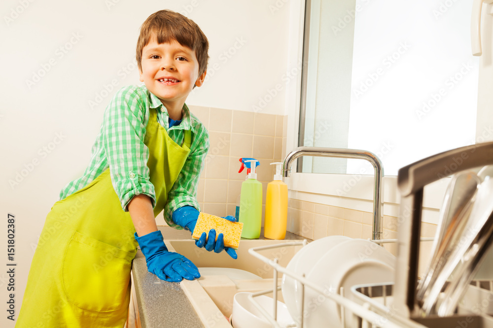 Happy boy wearing apron holding sponge in his hand