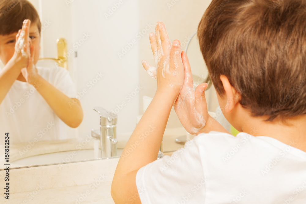 Boy washing hands with soap and looking in mirror