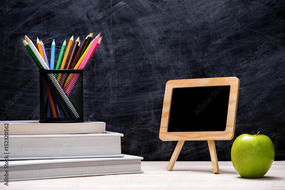 School and office supplies and apple in front of blackboard.