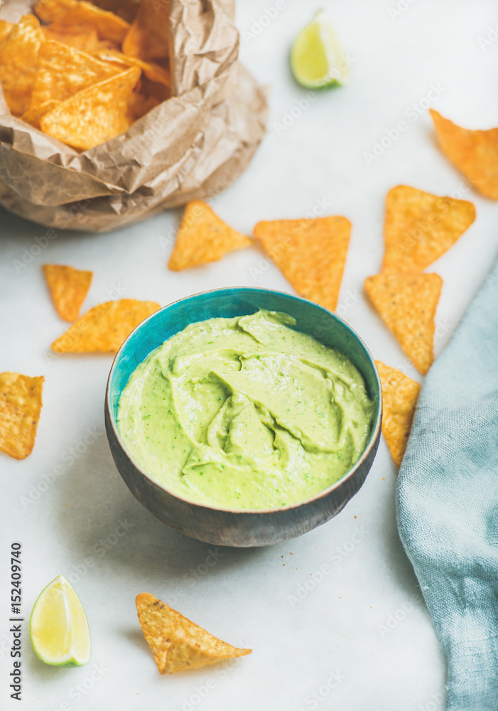 Mexican corn chips and fresh guacamole sauce over marble table background, selective focus, vertical