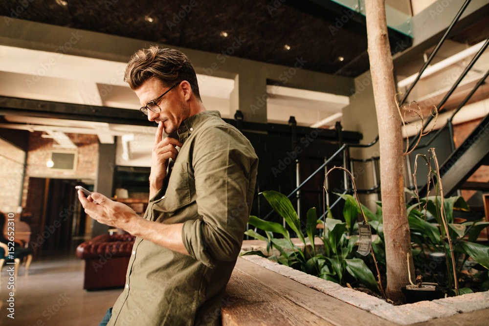 Thoughtful businessman using mobile phone in office lobby