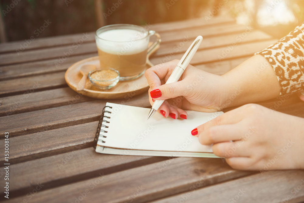 Womans hands writing on notebook , hot coffee and vintage wooden table background