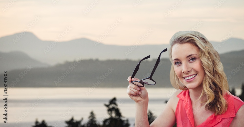 Happy woman holding eyeglasses with lake and mountains in background