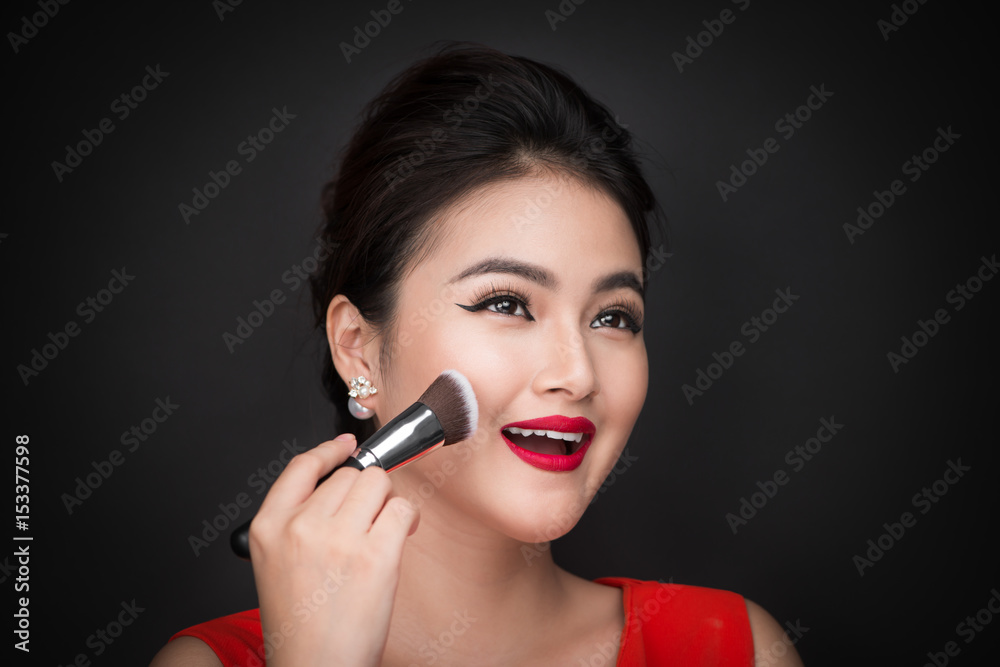 Cosmetic powder brush. Asian woman applying blusher on her cheeks with perfect make-up and red lips