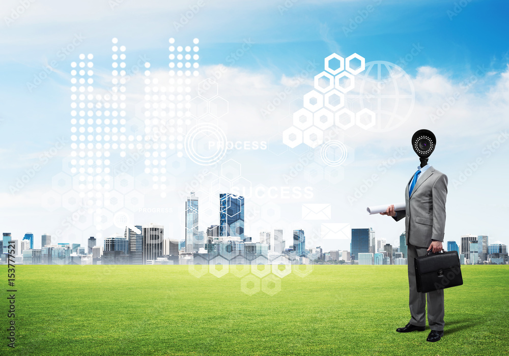 Camera headed man standing on green grass against modern cityscape