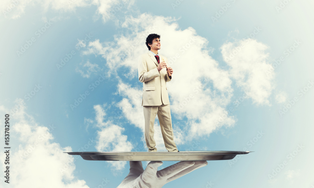 Businessman on metal tray playing fife against blue sky background