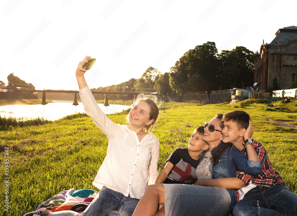 夏日一家人在公园里用智能手机自拍。夏日阳光明媚