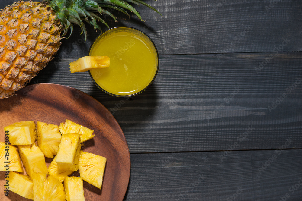 Top view of glasses of pineapple juice and pineapple fruit on a black wooden table