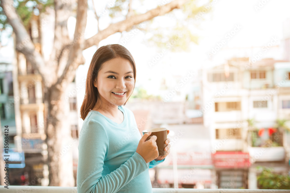 一个快乐的亚洲女人在早餐时拿着咖啡或茶杯思考的肖像