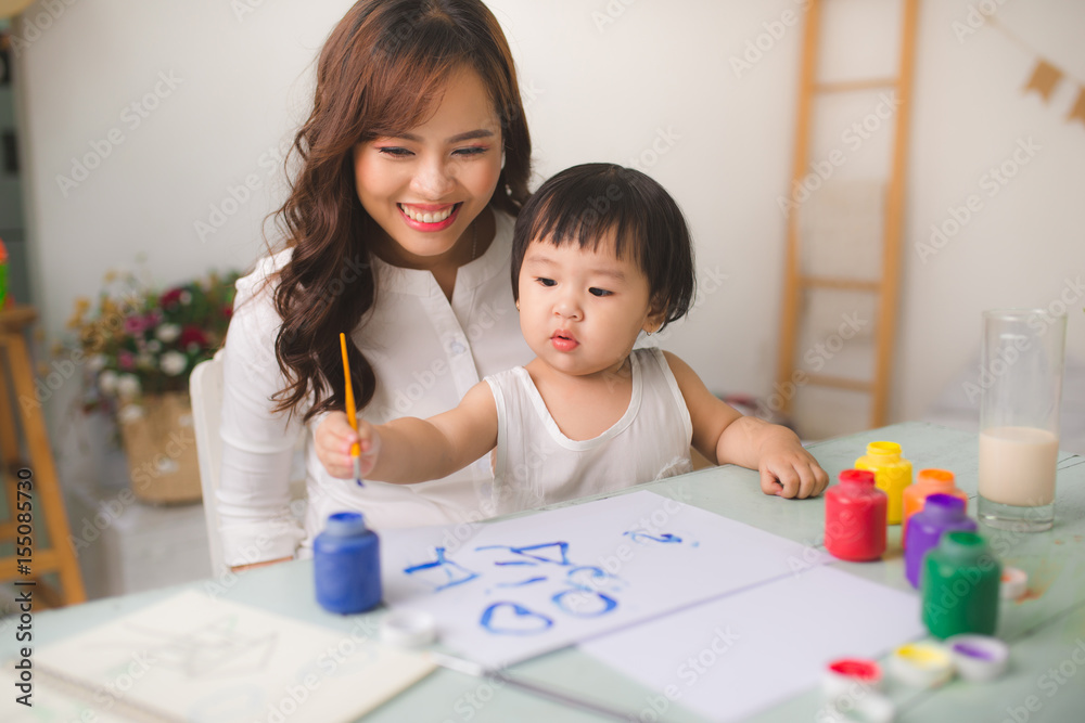 幸福的家庭，母亲和女儿一起画画。亚洲妇女帮助她的小女儿。