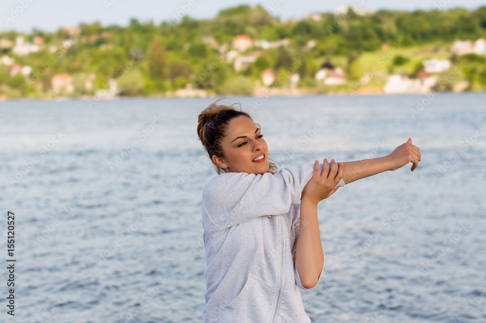 Beautiful young woman doing stretching exercises while standing outdoors