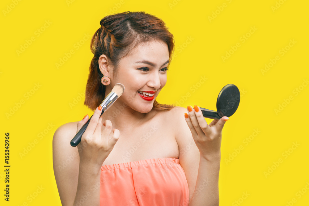 Portrait of Asian Beautiful woman with makeup brush near her face looking at mirror and smiling agai