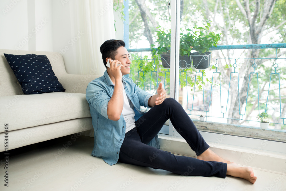 Thoughtful asian man listening to mobile phone in bedroom at home