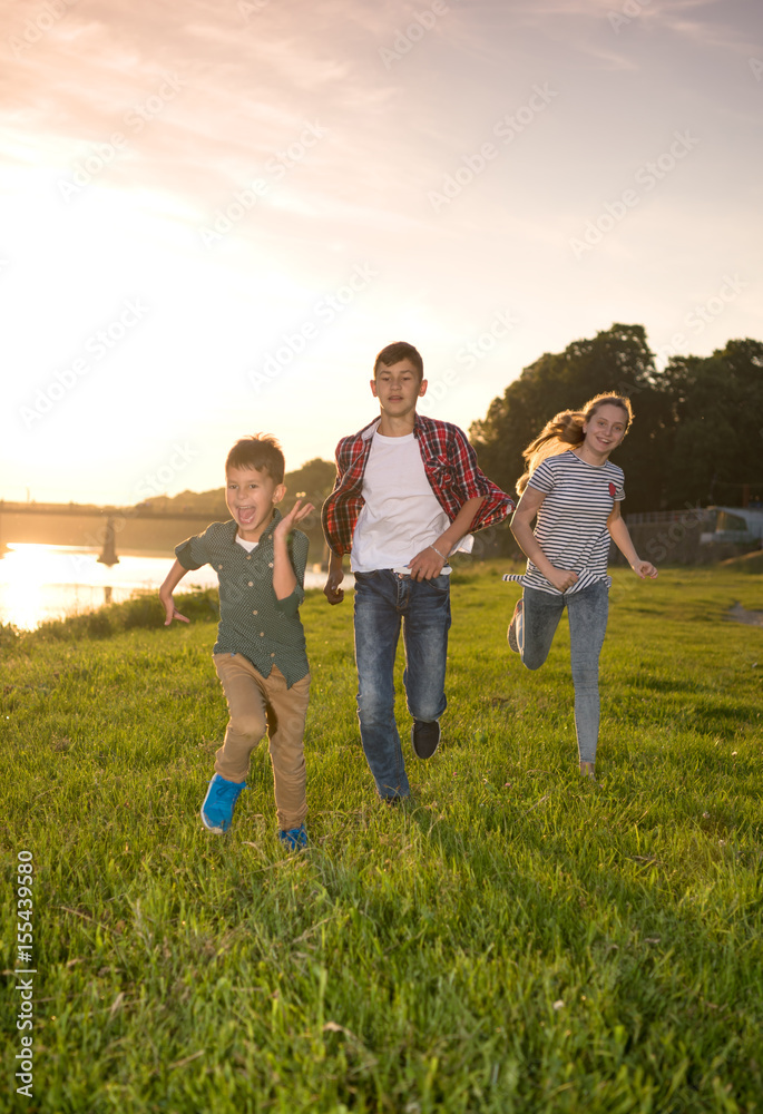 Group of happy friends playing catch-up game and running in summer park